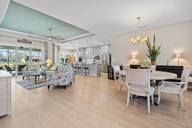 dining area with ceiling fan with notable chandelier, light hardwood / wood-style flooring, and a raised ceiling