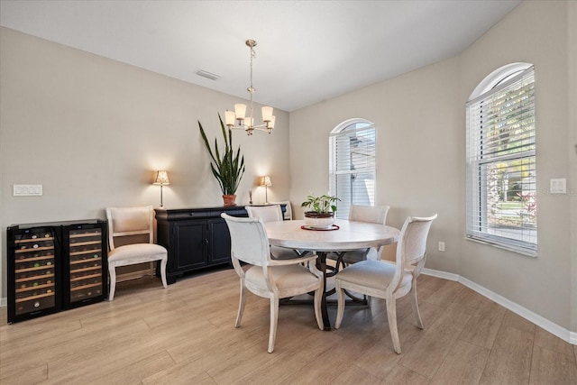 dining area featuring wine cooler, a healthy amount of sunlight, an inviting chandelier, and light hardwood / wood-style floors