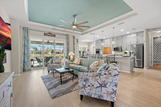 living room featuring ceiling fan, a tray ceiling, and light wood-type flooring