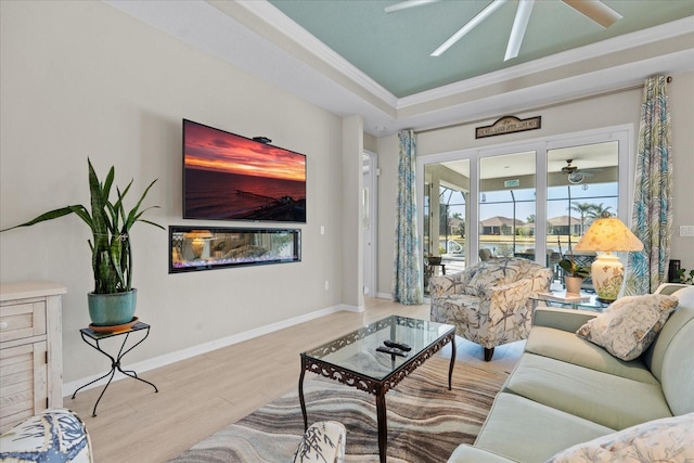 living room with crown molding, light hardwood / wood-style flooring, a raised ceiling, and ceiling fan