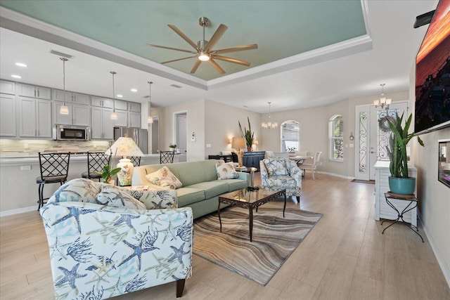 living room with a raised ceiling, ceiling fan with notable chandelier, and light hardwood / wood-style floors