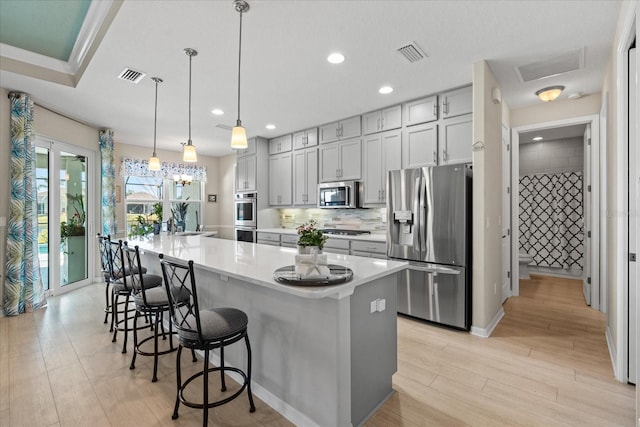 kitchen featuring stainless steel appliances, a spacious island, gray cabinets, and decorative light fixtures