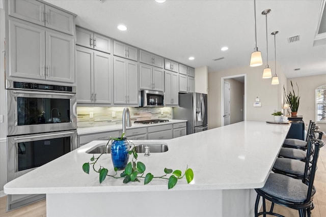 kitchen featuring a breakfast bar, sink, appliances with stainless steel finishes, pendant lighting, and a large island