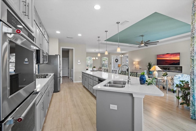 kitchen featuring sink, gray cabinetry, a center island with sink, decorative light fixtures, and a raised ceiling