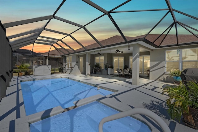 pool at dusk with ceiling fan, glass enclosure, and a patio area