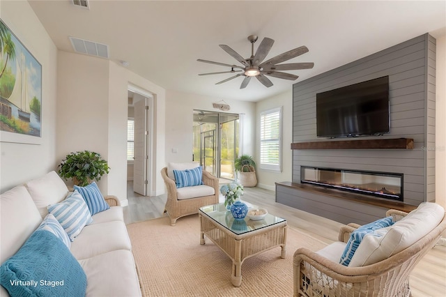 living room with light hardwood / wood-style floors, a large fireplace, and ceiling fan