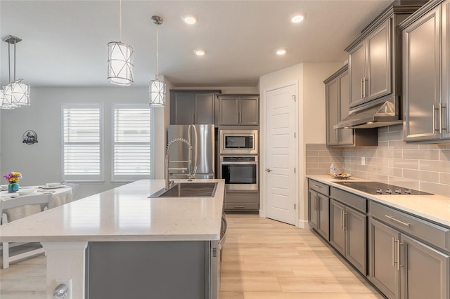 kitchen featuring sink, decorative light fixtures, stainless steel appliances, a kitchen island with sink, and backsplash