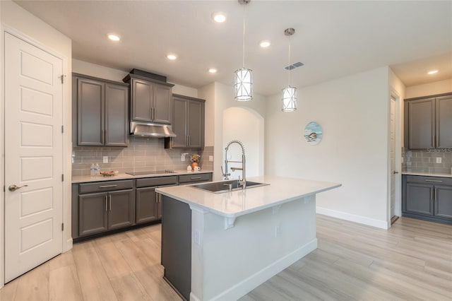 kitchen with decorative light fixtures, sink, black electric cooktop, a center island with sink, and light wood-type flooring