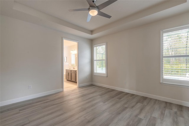 empty room featuring a tray ceiling, light hardwood / wood-style floors, and ceiling fan