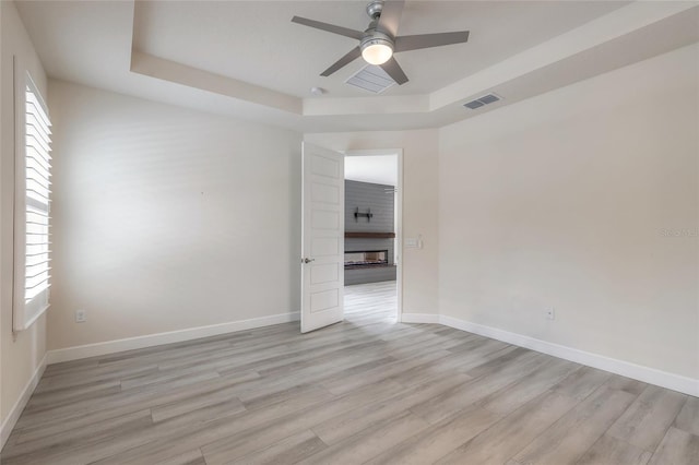 spare room with light hardwood / wood-style floors, a fireplace, and a tray ceiling