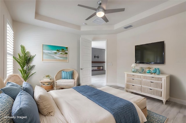 bedroom with light hardwood / wood-style flooring, ceiling fan, and a tray ceiling