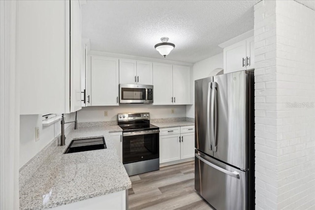 kitchen featuring sink, light stone counters, a textured ceiling, appliances with stainless steel finishes, and white cabinets