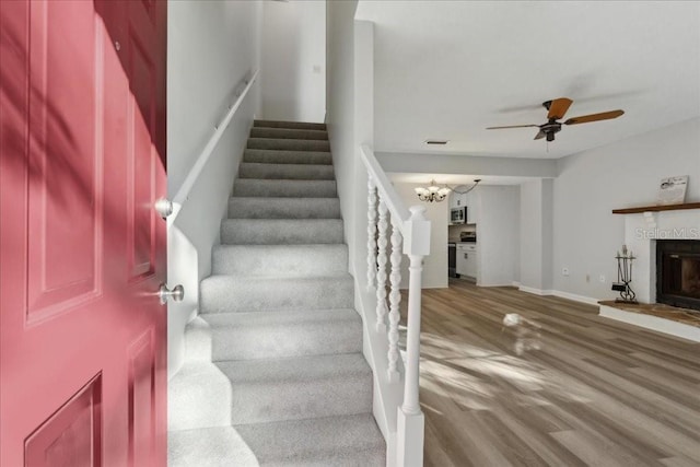 staircase with ceiling fan with notable chandelier and wood-type flooring