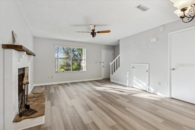 unfurnished living room with a brick fireplace, ceiling fan, a textured ceiling, and light wood-type flooring