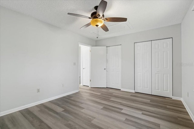 unfurnished bedroom with ceiling fan, a textured ceiling, light hardwood / wood-style flooring, and two closets