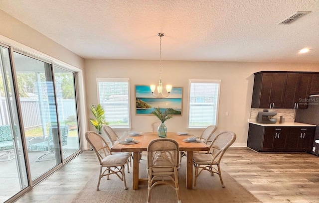 dining area with a chandelier, a wealth of natural light, a textured ceiling, and light wood-type flooring