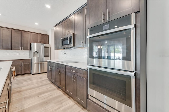 kitchen with stainless steel appliances, dark brown cabinetry, and light hardwood / wood-style flooring