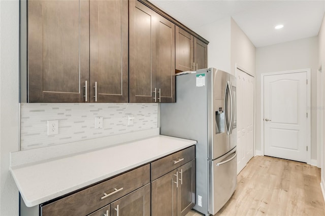 kitchen with dark brown cabinetry, decorative backsplash, light wood-type flooring, and stainless steel refrigerator with ice dispenser