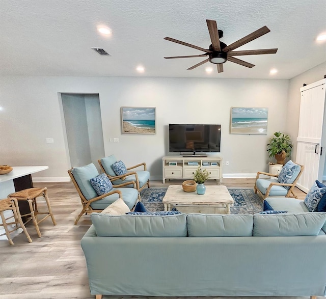 living room with ceiling fan, light hardwood / wood-style floors, and a textured ceiling