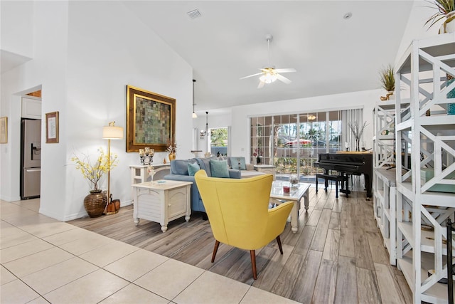 living room with ceiling fan with notable chandelier, high vaulted ceiling, and light hardwood / wood-style floors