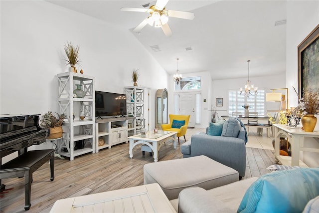 living room with ceiling fan with notable chandelier, high vaulted ceiling, and light hardwood / wood-style flooring