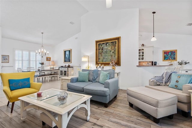 living room with high vaulted ceiling, a chandelier, and light wood-type flooring