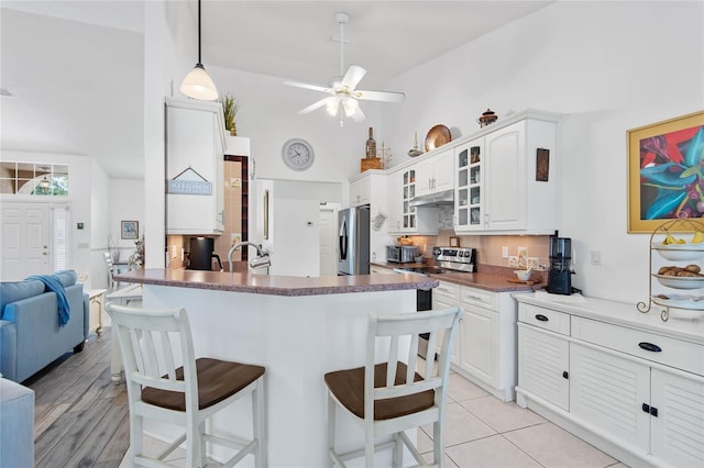 kitchen featuring tasteful backsplash, a kitchen breakfast bar, kitchen peninsula, stainless steel appliances, and white cabinets