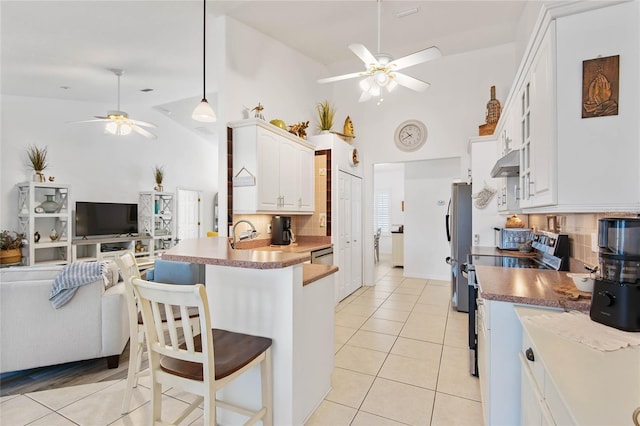 kitchen with ceiling fan, a kitchen bar, stainless steel appliances, white cabinets, and light tile patterned flooring