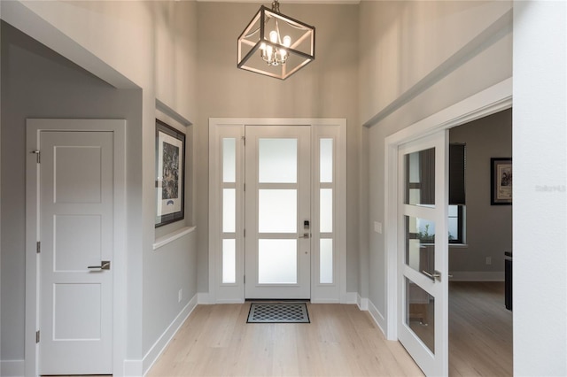 foyer entrance with a towering ceiling, light wood-style flooring, baseboards, and a notable chandelier