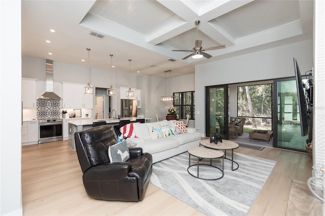 living room featuring light wood-style flooring, a high ceiling, coffered ceiling, visible vents, and beamed ceiling