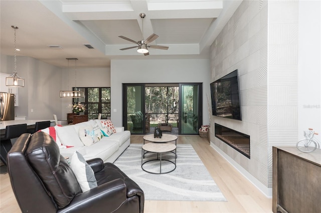 living area featuring light wood-style flooring, a fireplace, visible vents, and coffered ceiling