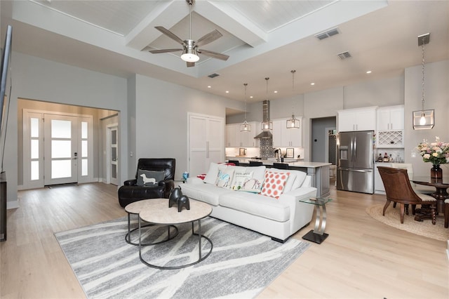 living area featuring light wood-type flooring, beam ceiling, visible vents, and a towering ceiling