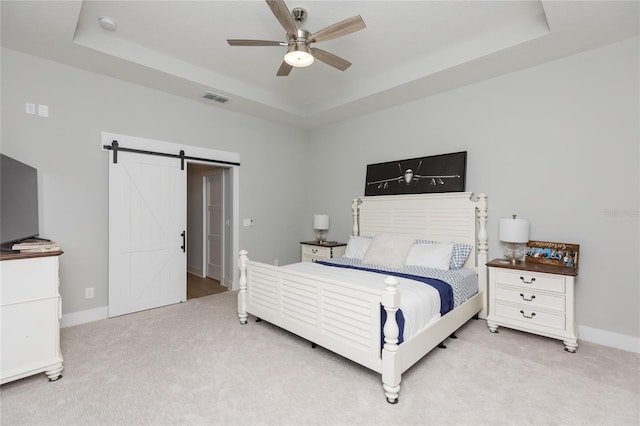 carpeted bedroom featuring a tray ceiling, visible vents, a barn door, ceiling fan, and baseboards