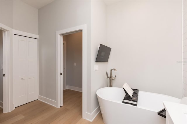 full bathroom with a closet, baseboards, a freestanding bath, and wood finished floors