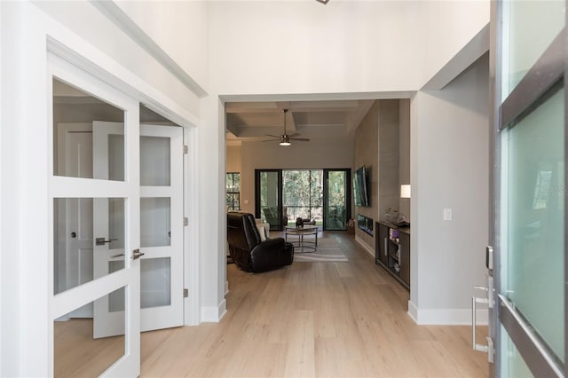 foyer entrance with baseboards, a ceiling fan, beam ceiling, and light wood finished floors
