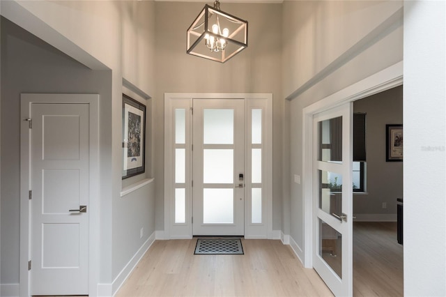 foyer entrance with light wood-type flooring, a towering ceiling, baseboards, and an inviting chandelier