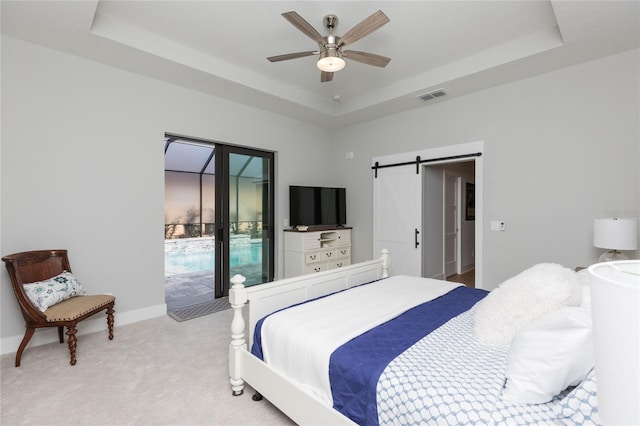 bedroom with a tray ceiling, a barn door, access to exterior, visible vents, and light colored carpet