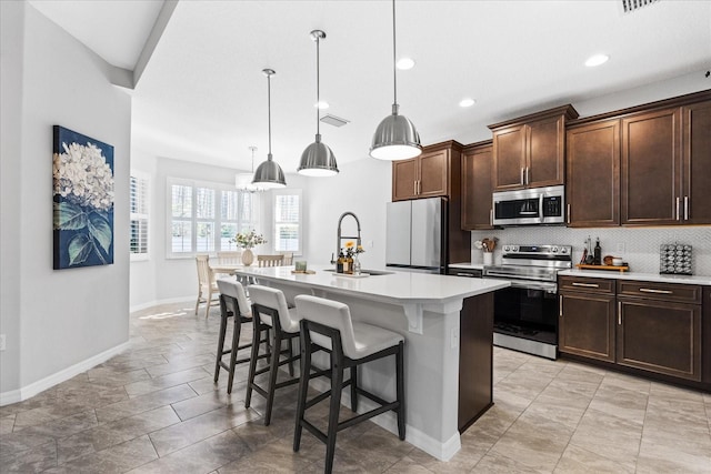 kitchen with pendant lighting, stainless steel appliances, sink, and a kitchen island with sink