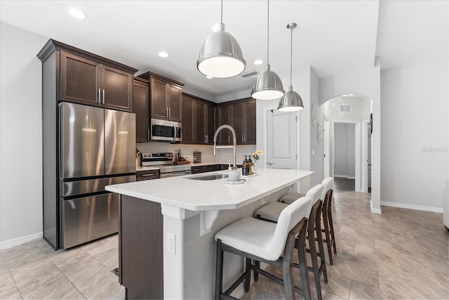 kitchen featuring appliances with stainless steel finishes, pendant lighting, sink, a kitchen island with sink, and dark brown cabinets