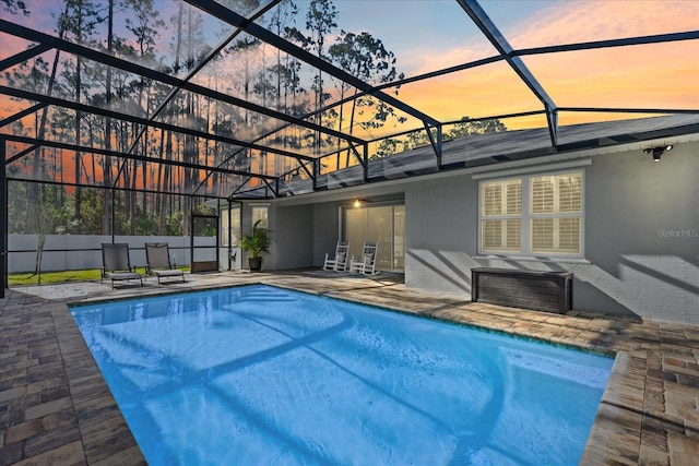 pool at dusk with a lanai and a patio area