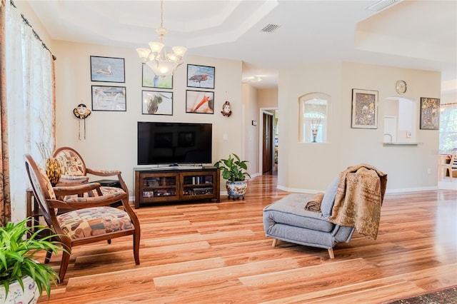 living room featuring a raised ceiling, a chandelier, and light wood-type flooring