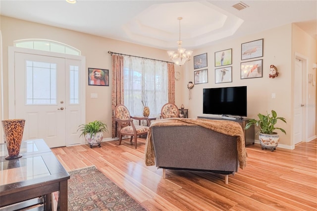 living room with a tray ceiling, hardwood / wood-style floors, and a notable chandelier