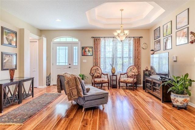 living area with a raised ceiling, a wealth of natural light, a chandelier, and light hardwood / wood-style flooring