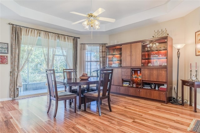 dining room with light hardwood / wood-style floors, a raised ceiling, and ceiling fan