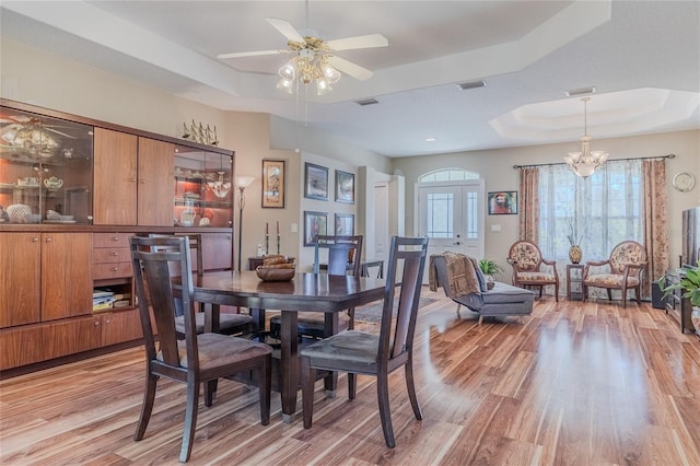 dining room with ceiling fan with notable chandelier, a raised ceiling, and light hardwood / wood-style floors