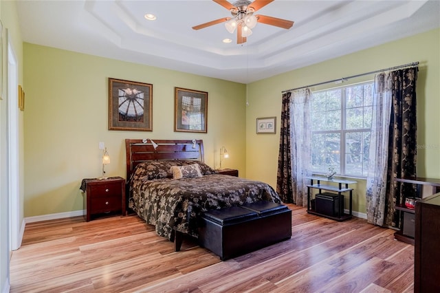 bedroom with ceiling fan, a tray ceiling, and light wood-type flooring