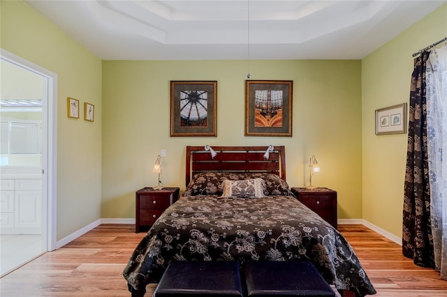 bedroom featuring ensuite bath, a raised ceiling, and light wood-type flooring