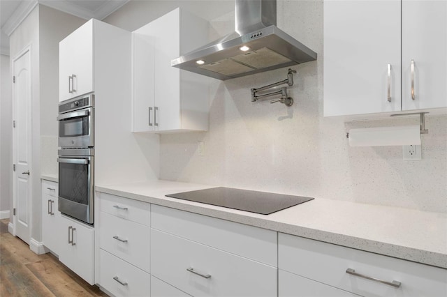 kitchen featuring black electric cooktop, stainless steel double oven, range hood, hardwood / wood-style floors, and white cabinets