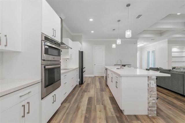 kitchen with decorative light fixtures, an island with sink, and white cabinets