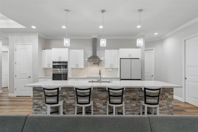 kitchen with refrigerator, wall chimney range hood, decorative light fixtures, and a center island with sink